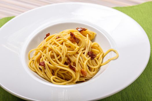 Italian delicious spaghetti carbonara pasta with bacon parmesan cheese garlic creamy sauce lies in a dark wooden round plate, bottle of olive oil, spices and a sprig of green leaves, top view close-up