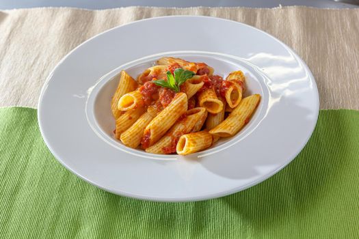 Serving of spicy savory italian penne pasta garnished with fresh basil and topped with grated Parmigiano-Reggiano, or parmesan, cheese