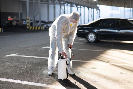 Man dressed white protective overalls spraying surface antibacterial sanitizer sprayer during quarantine Caucasian person protective suit prepares the equipment pumps the pump in the pump