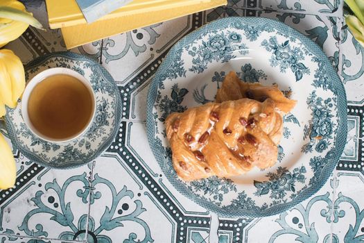 flat lay food, sweet puff, tea in a vintage porcelain cup and a stack of books, a bouquet of yellow withering tulips in a vase,. High quality photo