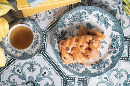 flat lay food, sweet puff, tea in a vintage porcelain cup and a stack of books, a bouquet of yellow withering tulips in a vase,. High quality photo