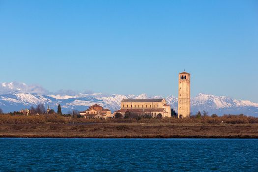 The coastline and high bell tower on the island of Burano with the snowy mountains behind