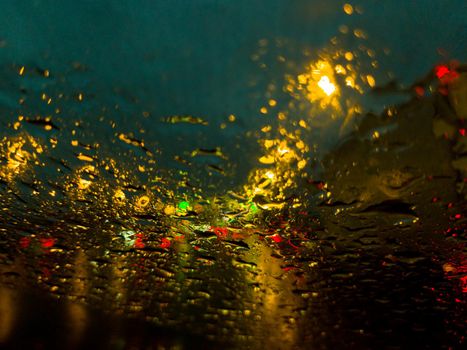 Raindrops on the windshield of the car. There is a lot of traffic, the lights of cars are reflected.