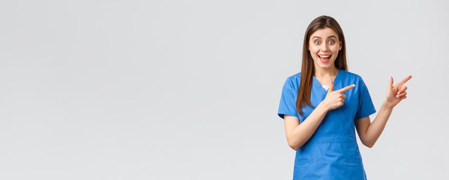 Healthcare workers, prevent virus, insurance and medicine concept. Excited happy female nurse or doctor in blue scrubs pointing fingers right, look amused, inform about promo or good news.