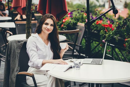 Young brunette woman using laptop computer sitting at cafe table and drik coffe. . Business People Concept