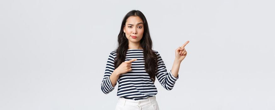 Lifestyle, beauty and fashion, people emotions concept. Skeptical and doubtful asian girl smirk unsatisfied as pointing fingers upper right corner, asking question as having doubts.