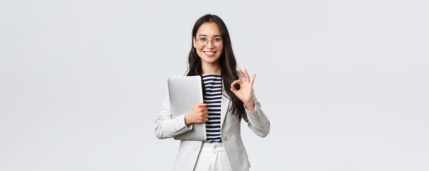 Business, finance and employment, female successful entrepreneurs concept. Young confident businesswoman in glasses, showing okay gesture, hold laptop, guarantee best service quality.