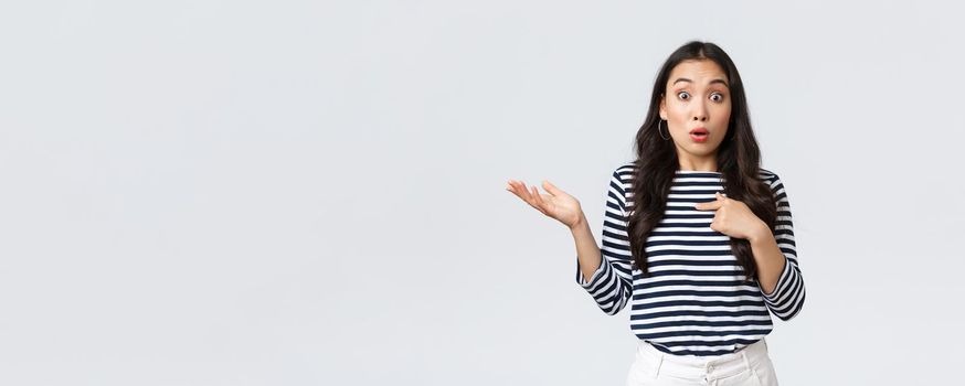 Lifestyle, beauty and fashion, people emotions concept. Shocked and surprised girl pointing at herself and shrugging as was picked or chosen, standing white background.