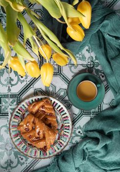 flat lay food, sweet puff, tea in a vintage porcelain cup and a stack of books, a bouquet of yellow withering tulips in a vase,. High quality photo