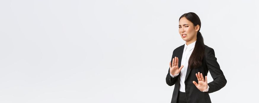 Displeased asian businesswoman avoiding risky suggestions, shaking hands in refusal, rejecting disgusting strange offer. Saleswoman grimacing from aversion and step away, white background.