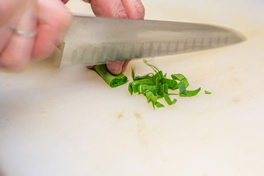 The cook very quickly cuts parsley leaves rolled into a tube with a knife on a white board.