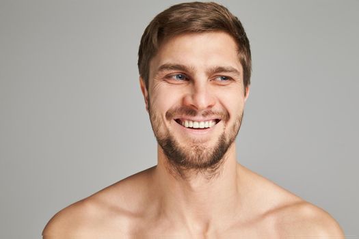 Portrait of a smiling young man with bare swimmers shoulders on a gray background, powerful, beard, charismatic, adult, brutal, athletic, edited photo, bright smile, white teeth smile, look in camera. High quality photo