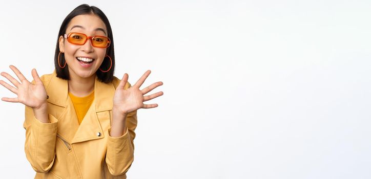 Surprised jazz hands. Happy asian girl smiling, looking amazed at camera, announcing smth, standing over white background.