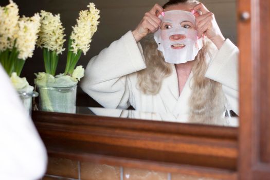 a middle-aged woman is busy with morning hygiene, trying in vain to straighten the mask with cleansing and moisturizing impregnation on her face High quality photo