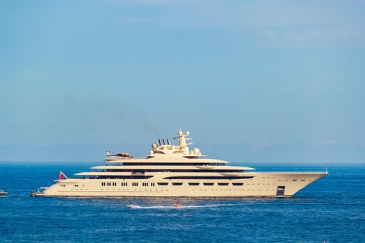 The huge beige mega yacht is moored in sea at sunny day, the chrome plated handrail, sun reflection on glossy board of the motor boat. High quality photo