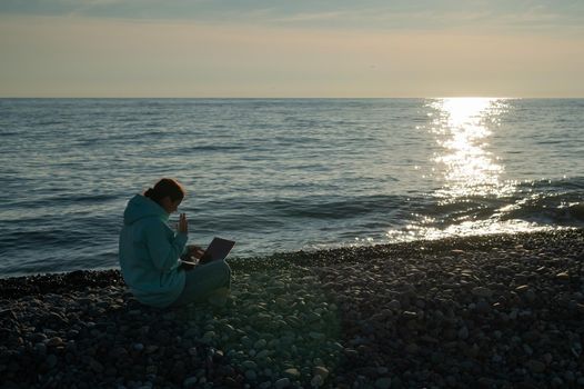 Caucasian woman communicating by video call on laptop on pebble beach