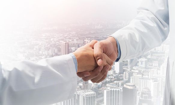 Close-up of the handshake between the two medics. Against the backdrop of the cityscape