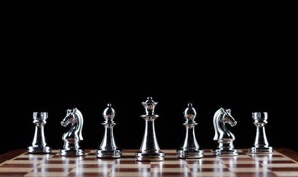 Silvery chess figures standing on chessboard. Intellectual competition and fight in business. Strategy planning and leadership concept with copy space. Silver chess pieces in row on black background.