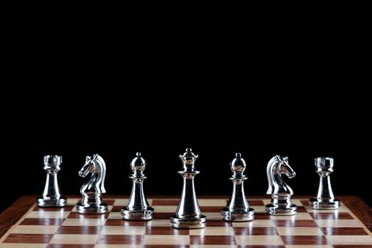 Silvery chess figures standing on chessboard. Intellectual competition and fight in business. Strategy planning and leadership concept with copy space. Silver chess pieces in row on black background.