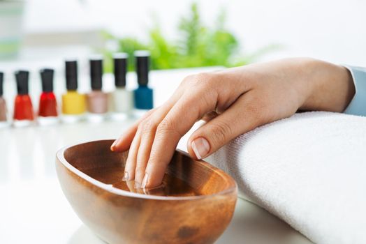 Closeup female hand in wooden bowl with water. Spa procedure and relaxation. Female hand preparing for manicure. Professional nail care and beautician service. Beauty and hygiene concept