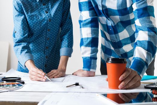 Man and woman together working at design project. Creative teamwork at workspace with construction blueprint and color swatches. People standing near desk and discussing in architecture studio.