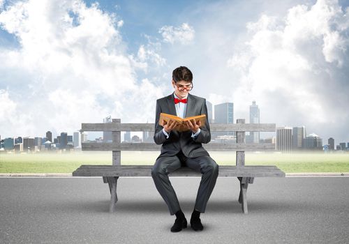 a young student with a book sits on a bench