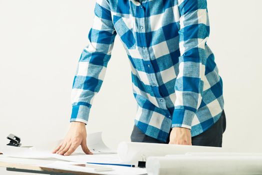 Architect standing near desk with paper blueprints. Architecture studio concept with design project. Close up man hand lying on construction drawing. Professional building, engineering and renovation