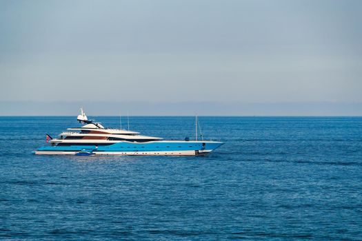 The huge mega yacht is moored in sea off the coast of the azur coastline at sunny day, the chrome plated handrail, sun reflection on glossy board of the motor boat. High quality photo