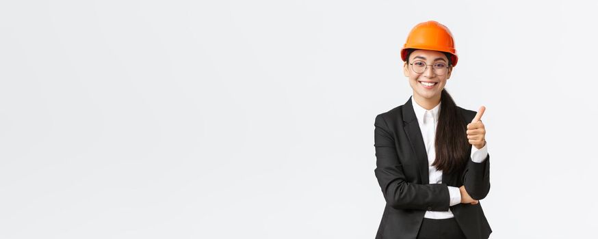 Satisfied female asian entrepreneur inspect enterprise, being pleased with construction work, showing thumbs-up in approval, smiling delighted, say well done, good job, guarantee finish build in time.