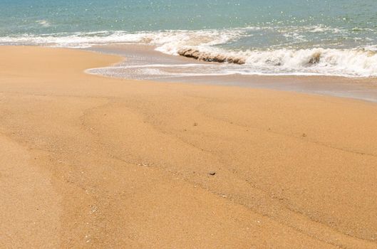 Blue sea waves with foam on yellow sand beach