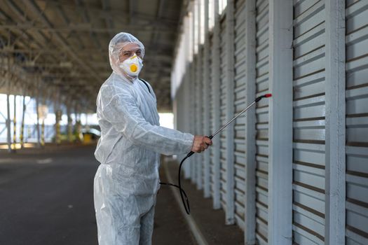 Worker wearing protective suit disinfection gear disinfect surface public place parking. Side view of disinfector safety overall and respiratory mask Covid pandemic disinfection preventive measures