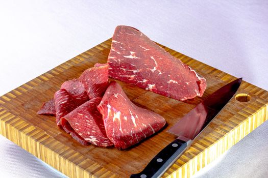 Roast beef. Thin slices of raw marbled beef lie on the board.