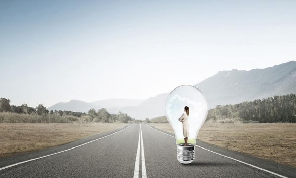 Young businesswoman trapped inside of light bulb on asphalt road