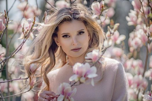 Portrait of a beautiful happy middle aged woman enjoying the smell in a blooming spring garden. Beautiful magnolia bushes, large flowers