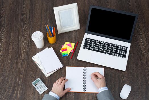 Businessman makes notes in notepad, top view workplace