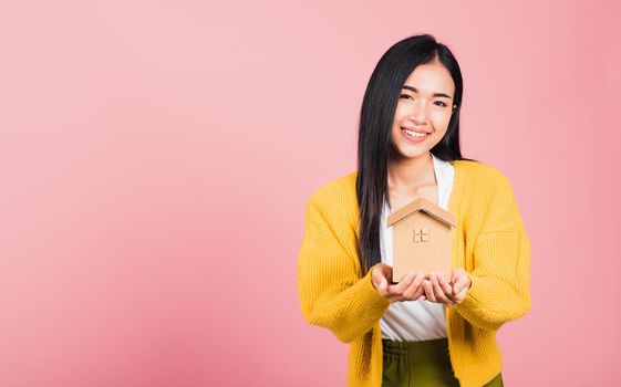 Happy Asian portrait beautiful cute young woman excited smiling holding house model on hand, studio shot isolated on pink background, broker female hold home real estate insurance and banking concept