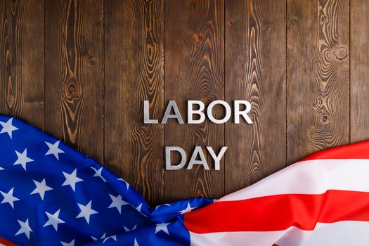 words labor day laid with silver metal letters on wooden surface with crumpled USA flag on bottom side in directly above high angle view