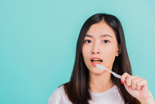 Asian beautiful young woman teen brushing teeth in the morning, portrait of happy Thai female confident smiling holding toothbrush, studio shot isolated on blue background, Dental health concept