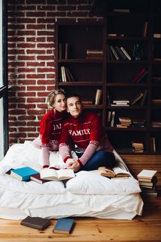 Beautiful smiling couple in red sweaters listening music, girlfriend leaning on handsome boyfriend, when he playing at gitar. Celebrating new year and xmas. Romantic winter holidays.