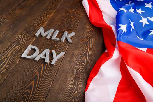 the word MLK day laid with silver metal letters on wooden surface with crumpled USA flag at right side in diagonal perspective. MLK means Martin Luther King Jr.