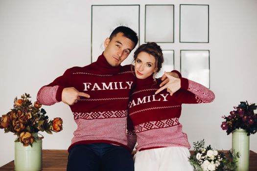 Beautiful smiling couple in red sweaters listening music, girlfriend leaning on handsome boyfriend, when he playing at gitar. Celebrating new year and xmas. Romantic winter holidays.