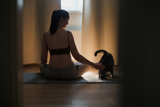 Young woman practices yoga and meditation at home with her cat. Doing exercises at home. Meditation and mental health concept