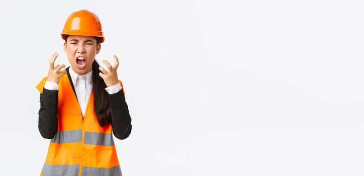 Mad and outraged asian female chief engineer, construction manager burst in rage, losing temper at employees, shouting and shaking hands aggressive, scream furious as scolding someone.