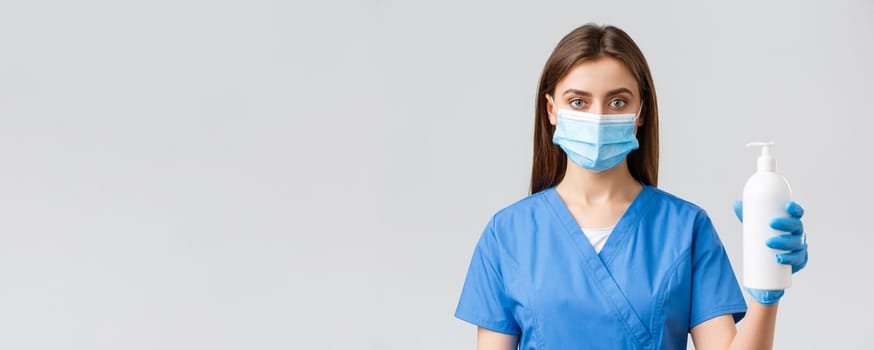 Covid-19, preventing virus, health, healthcare workers and quarantine concept. Serious-looking medical worker, nurse or doctor in blue scrubs and medical mask, showing hand sanitizer or soap.