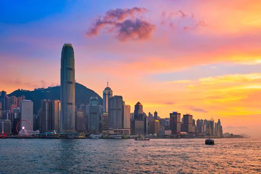 Hong Kong skyline cityscape downtown skyscrapers over Victoria Harbour in the evening with junk tourist ferry boat on sunset with dramatic sky. Hong Kong, China