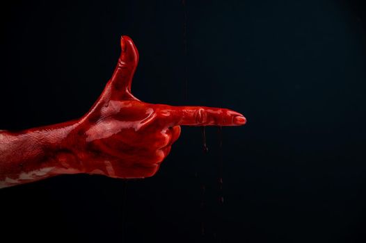 Woman's hand in blood shows a gesture of a gun on a black background