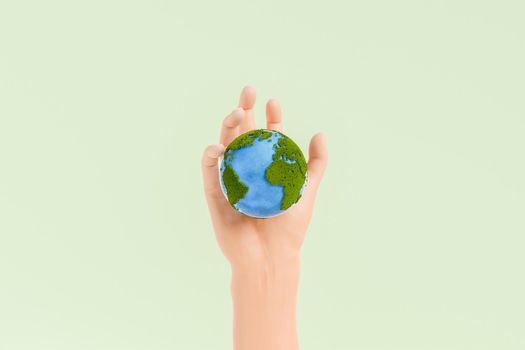 Hand of person holding small planet Earth covered with green moss and blue oceans on clear light background in studio. 3d rendering