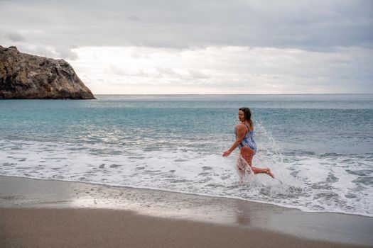 A plump woman in a bathing suit enters the water during the surf. Alone on the beach, Gray sky in the clouds, swimming in winter