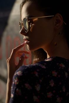 Close-up portrait of stylish young woman. Brunette in sundress posing on street. Finger near her lips