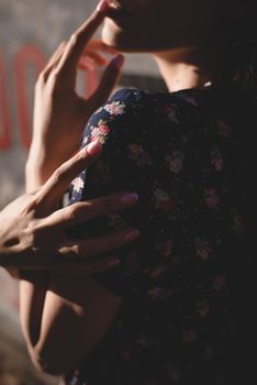 Close-up portrait of stylish young woman. Brunette in sundress posing on street. Finger near her lips